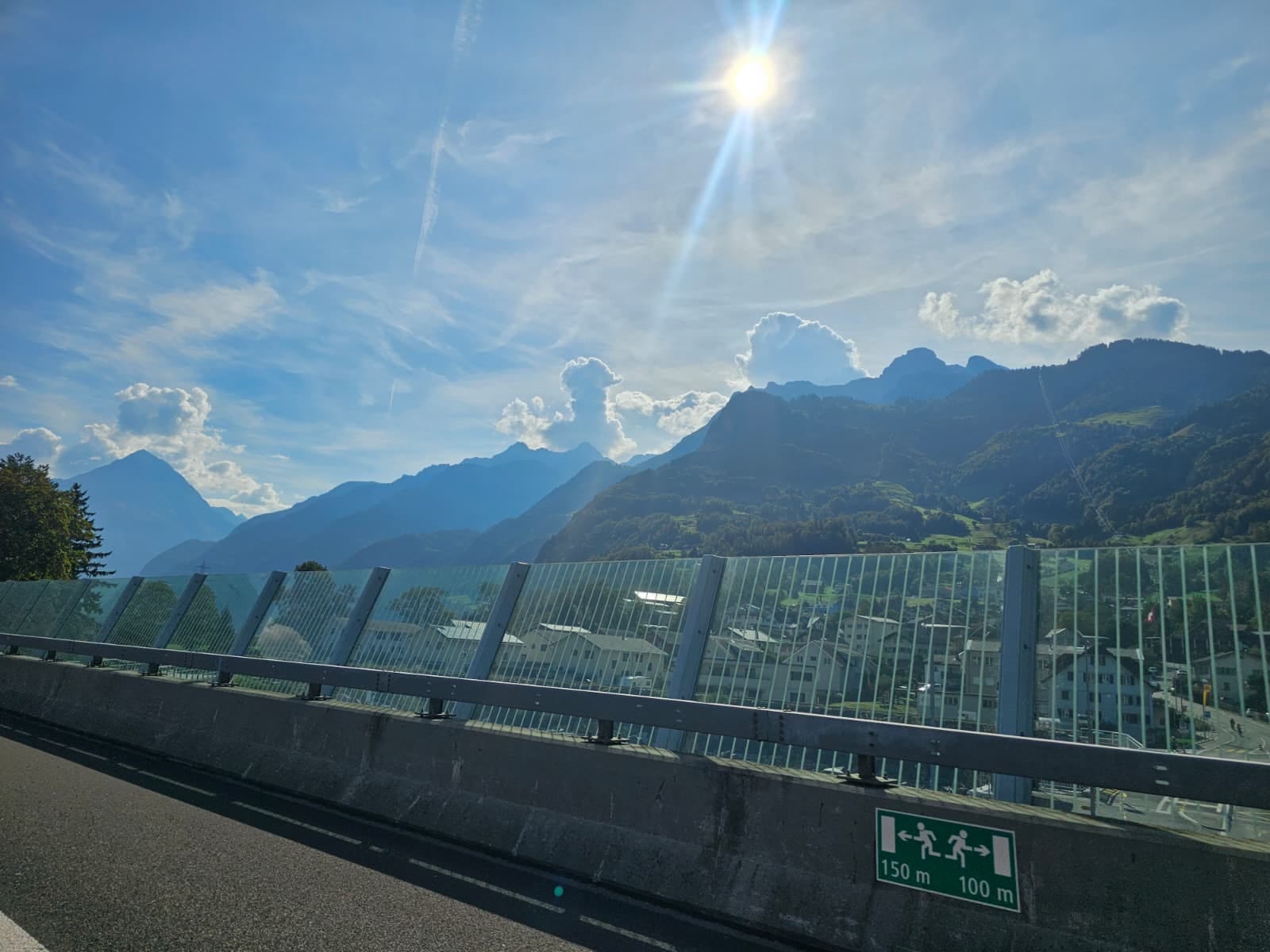 Autobahn mit Glas-Lärmschutzwand, Berge im Gegenlicht