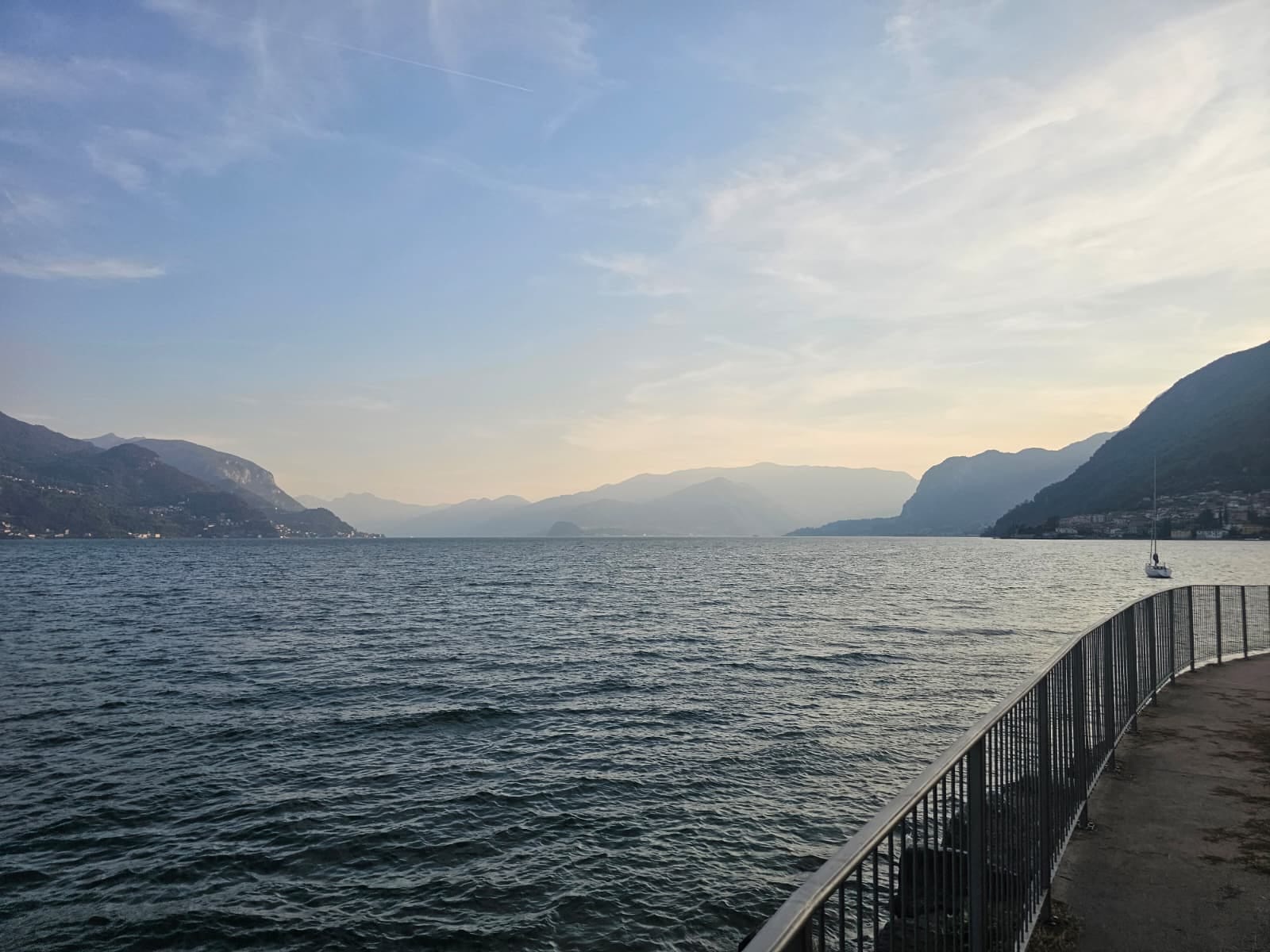 Der Comer See von der Uferpromenade, Segelboot und Berge im Abendlicht