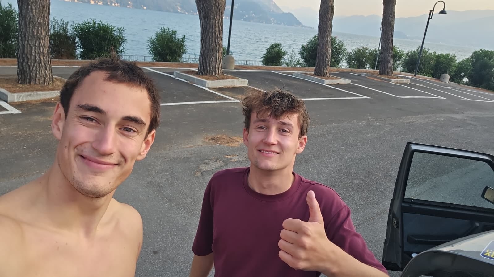 Selfie am Parkplatz am See, Daumen hoch neben der offenen Autotür